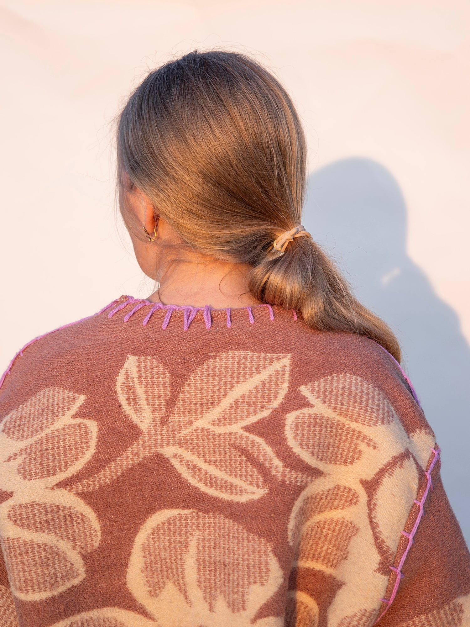 Person wearing a brown upcycled long wool blanket coat with a neutral background