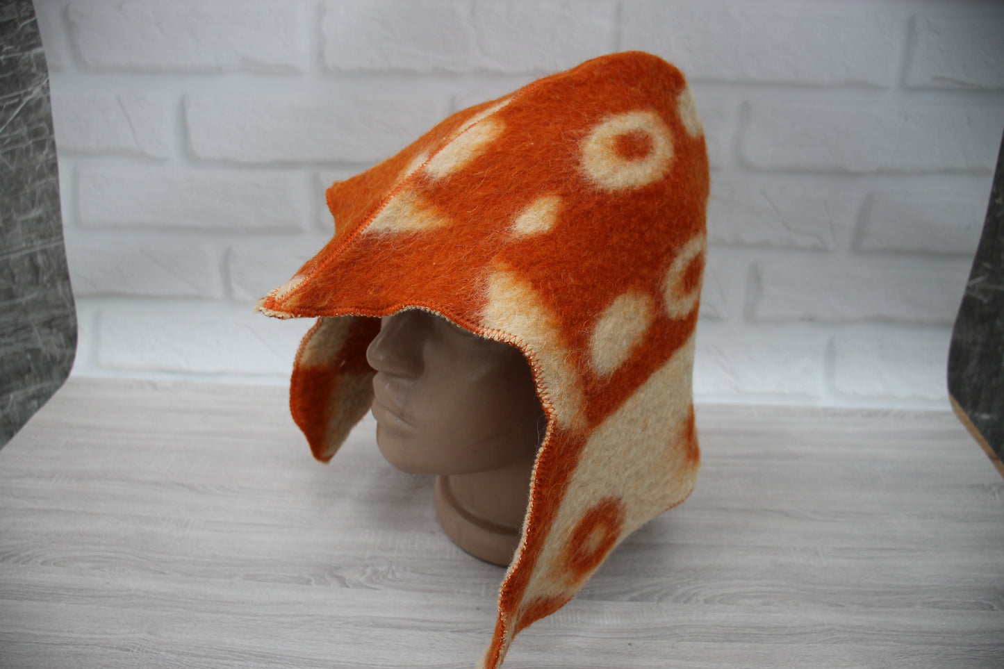Mannequin head wearing an orange and white patterned hat against a white brick wall.