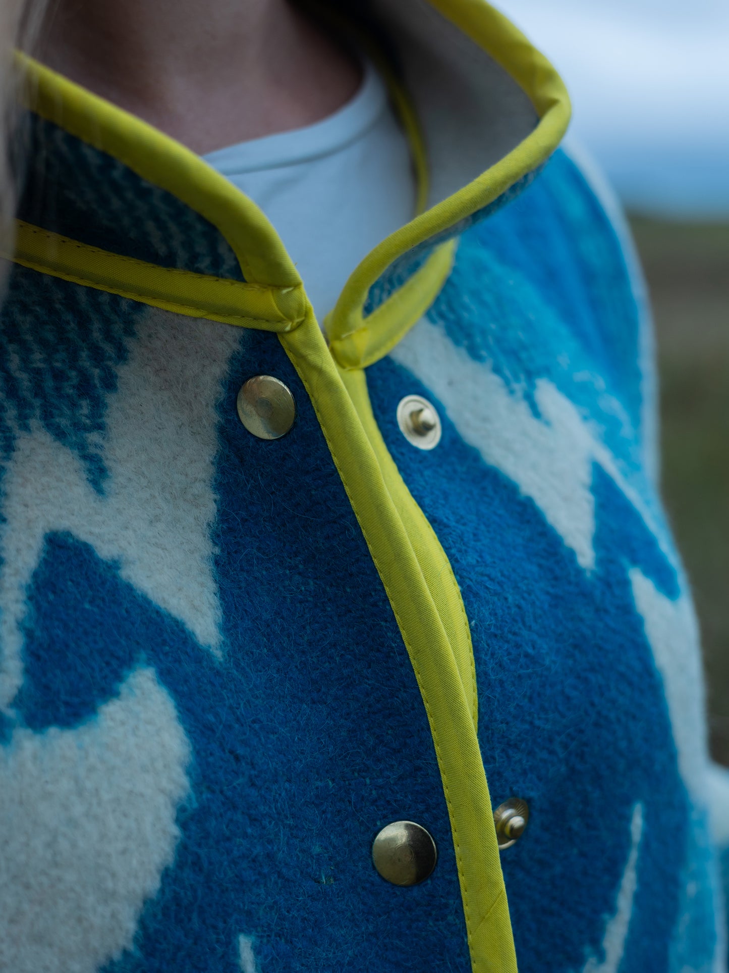 Close-up of a blue upcycled coat with yellow trim and gold buttons.