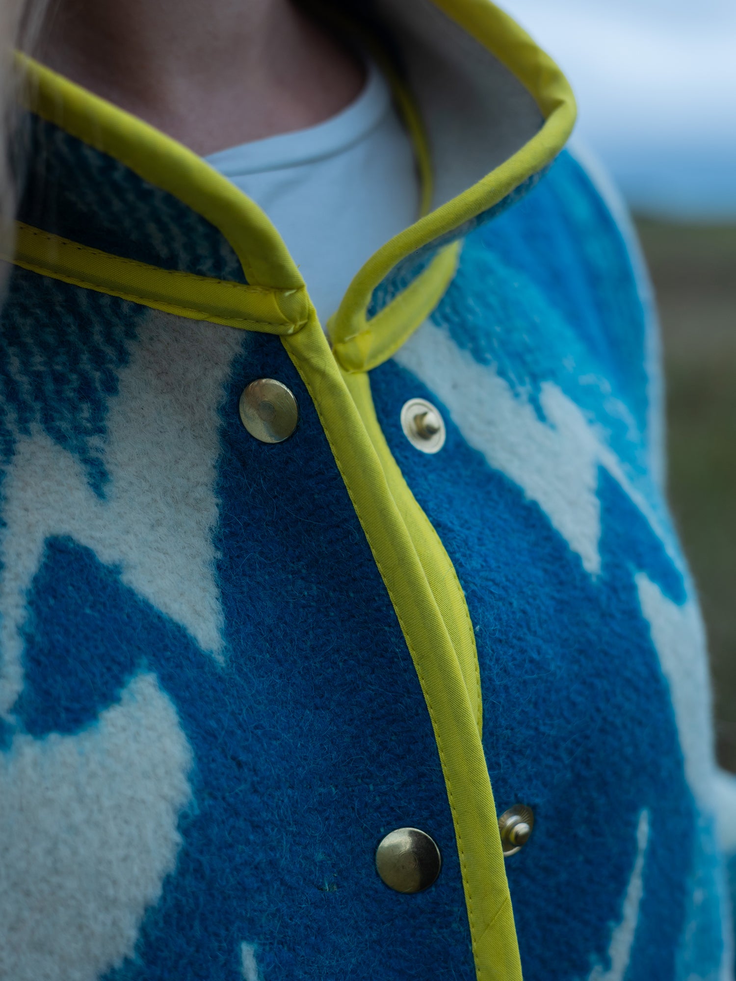 Close-up of a blue upcycled coat with yellow trim and gold buttons.