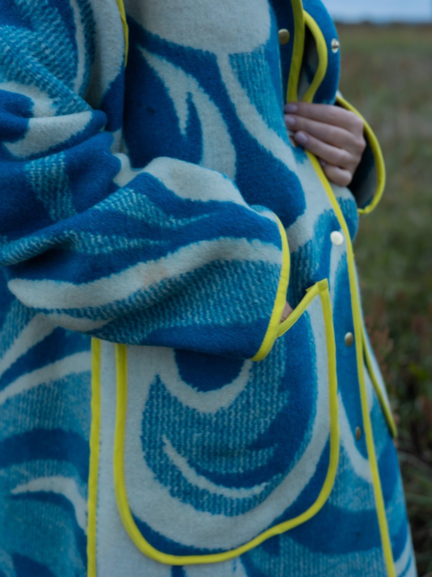 Close-up of a blue and white patterned upcycled blanket coat with yellow trim.